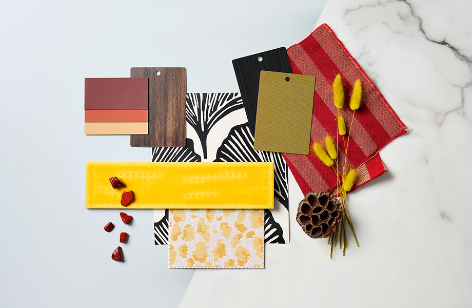 Échantillons rectangulaires de surfaces orangés, dorés, métalliques et grains de bois avec un tissu à rayures rouges et un bout de plante jaune séchée dans un agencement de palette de designer