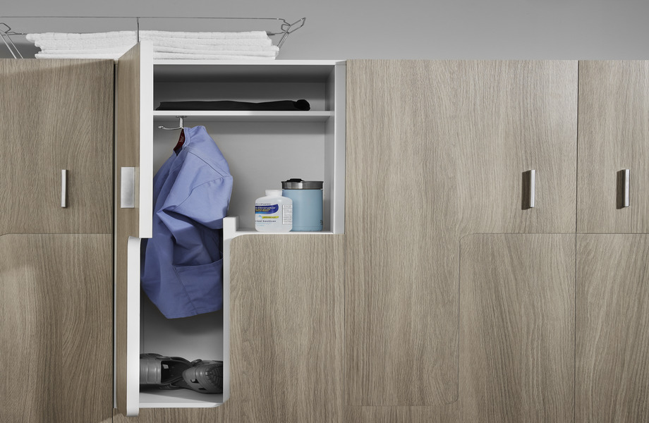 Casier en stratifié grains de bois Chêne Grisé dont la porte ouverte laisse entrevoir une blouse bleue, du désinfectant pour les mains et une bouteille d’eau
