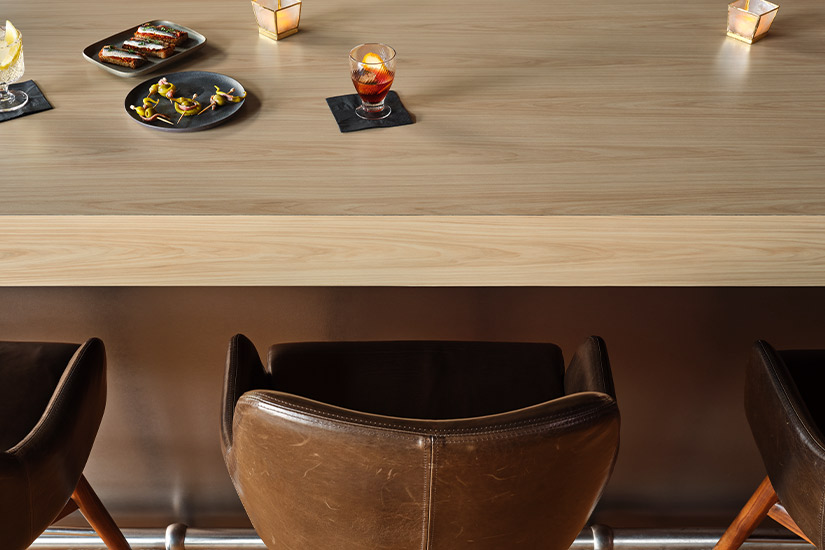 Un comptoir épais en stratifié de marque Formica® à grains de bois, Hickory Naturel Raffiné (9041) et la façade d’un bar en stratifié métallique Homapal® Maille Bronze (M6486).